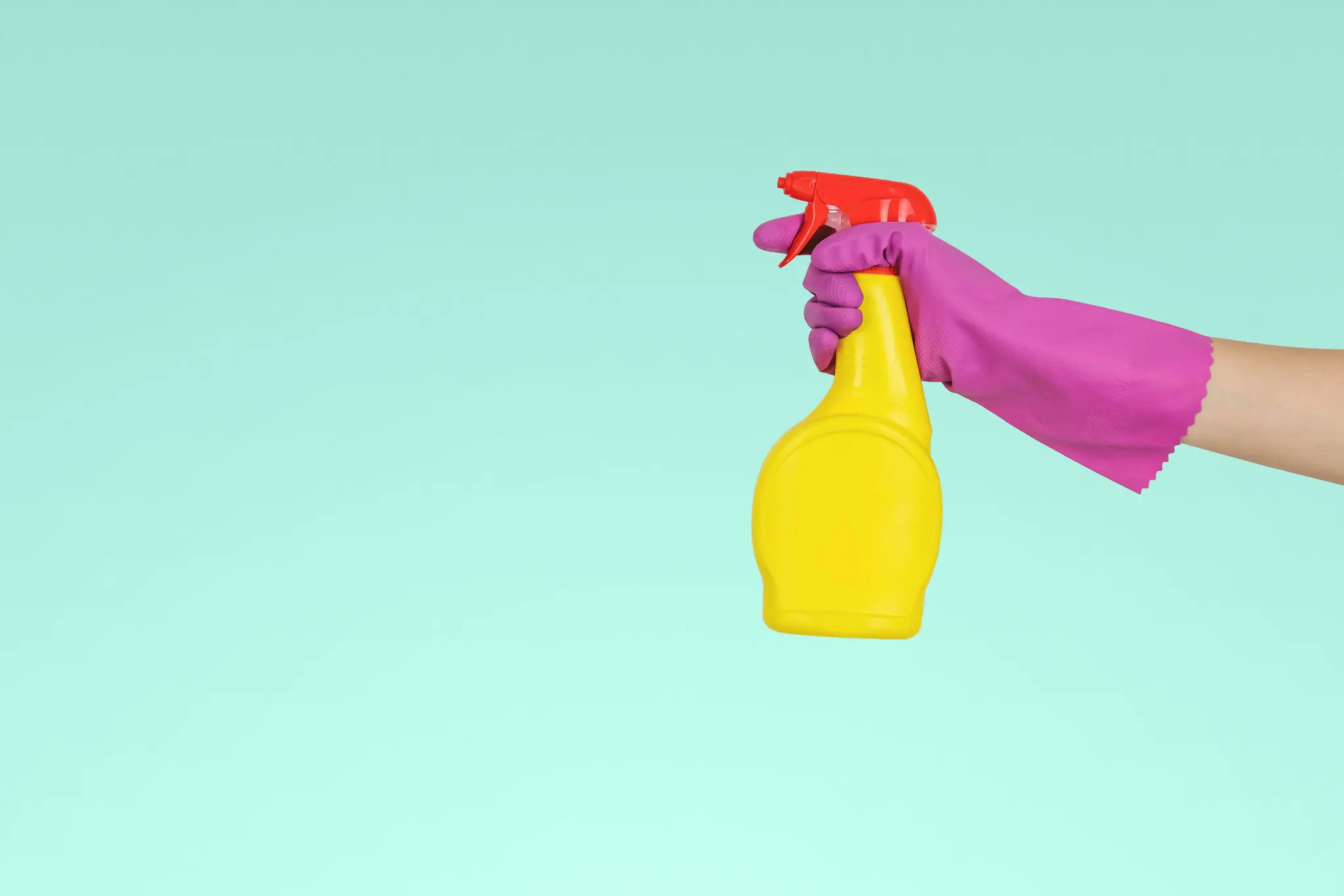 Hand in a pink rubber glove holding a yellow spray bottle