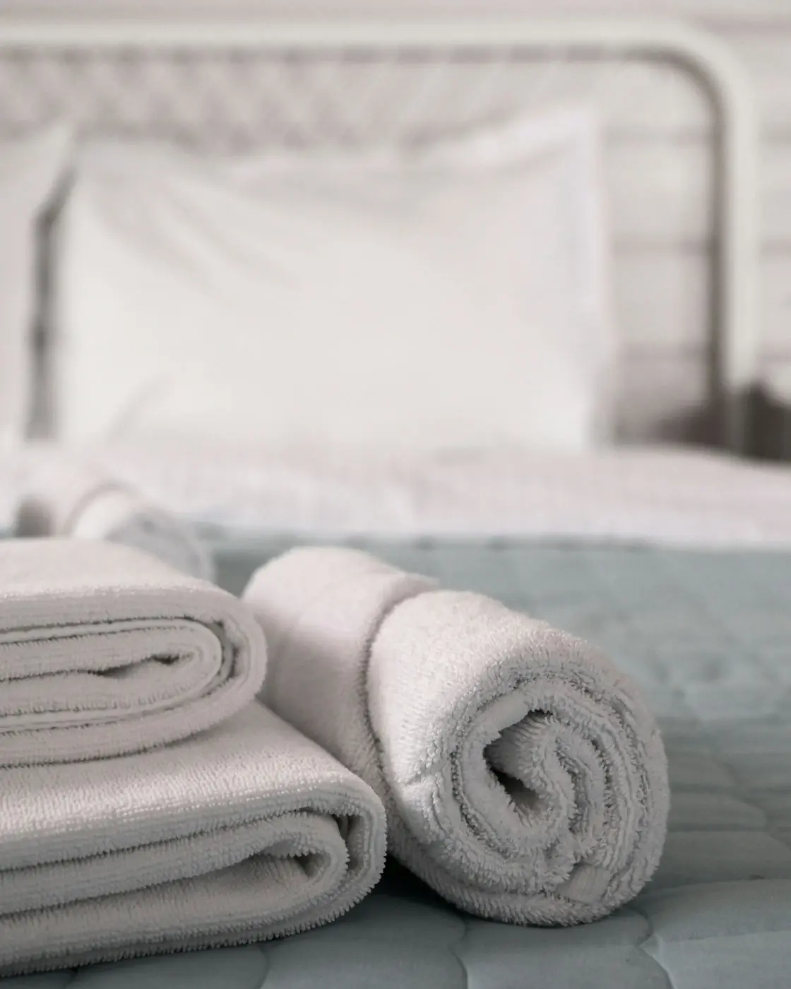 White towels, folded and rolled, on a made bed