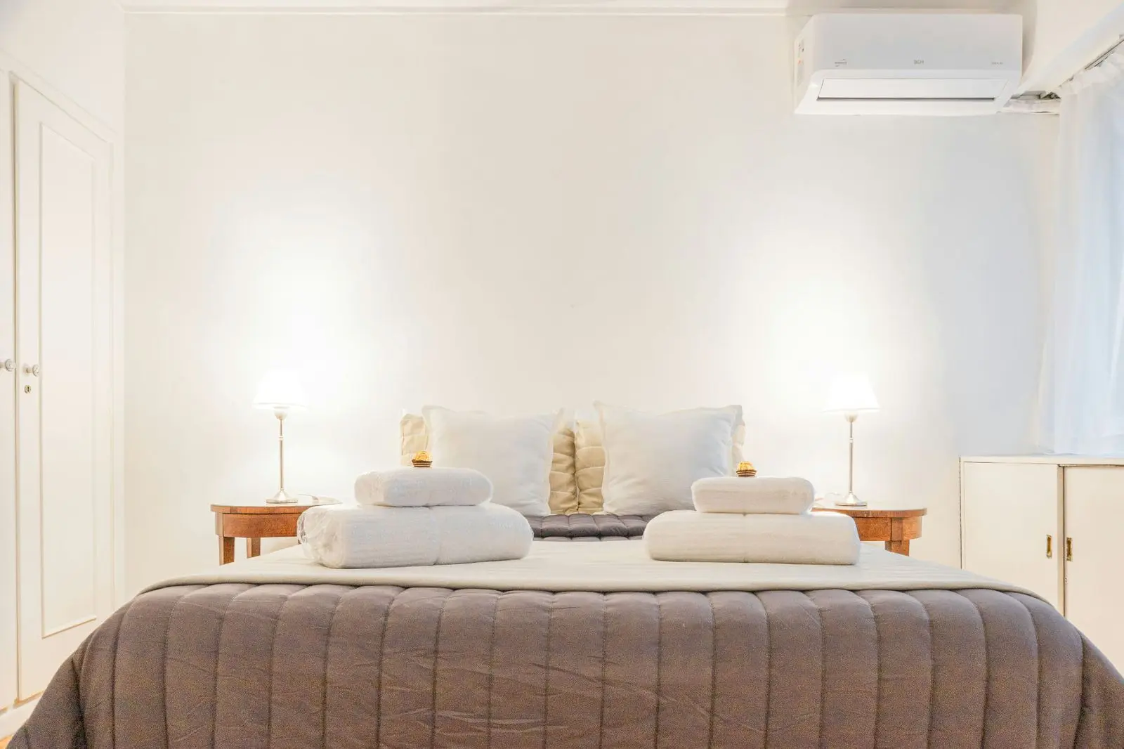 Bright bedroom with folded towels on the bed and two bedside tables with lamps