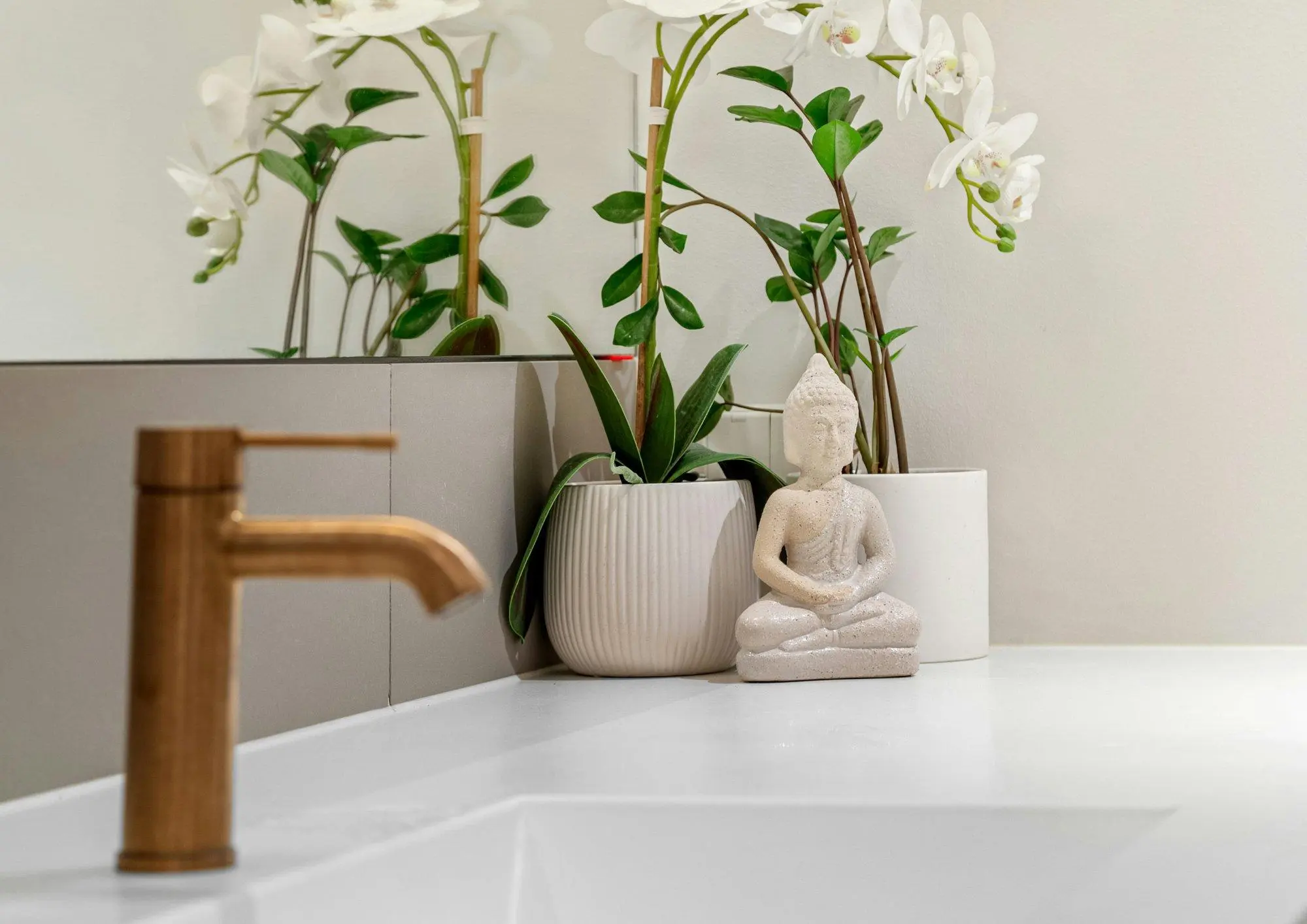 Brass tap over a white basin with orchids and a small Buddha figure