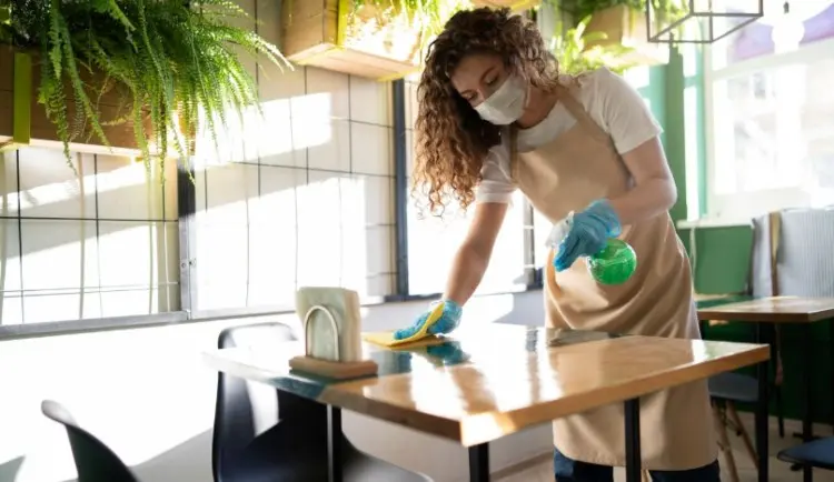 Camarera con mascarilla desinfectando una mesa de un restaurante