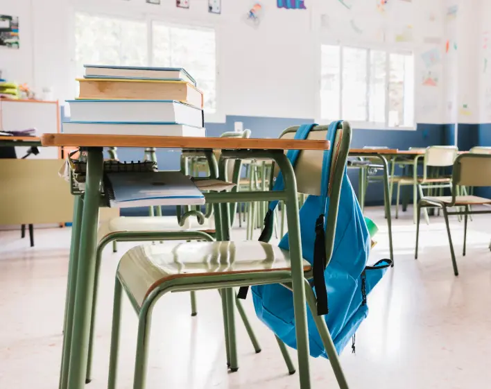 Aula escolar con pupitres, sillas y una mochila colgada