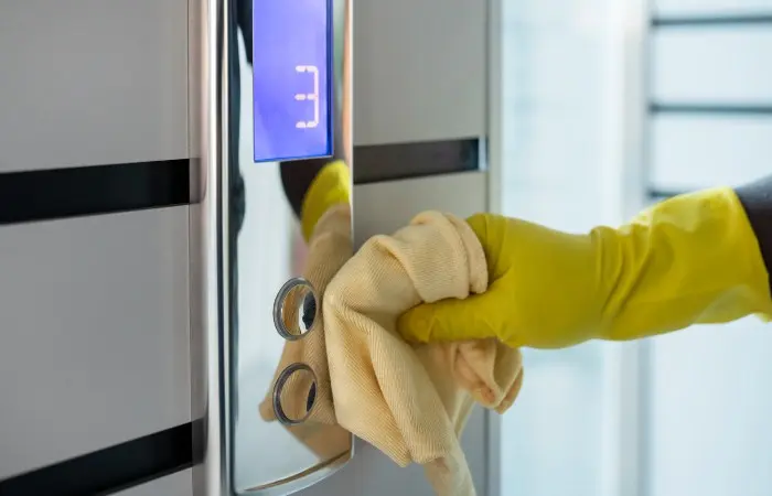 Yellow-gloved hand cleaning a lift's control panel