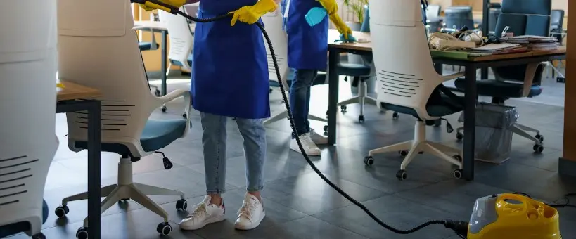 Two people cleaning an office, one of them vacuuming